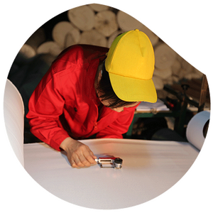 Mitarbeiterin prüft mit Lupe die Oberfläche eines weißen Stoffes in der Textilproduktion.