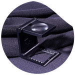 Fadenzähler-Lupe auf dunklem Stoff zur Prüfung der Gewebestruktur.